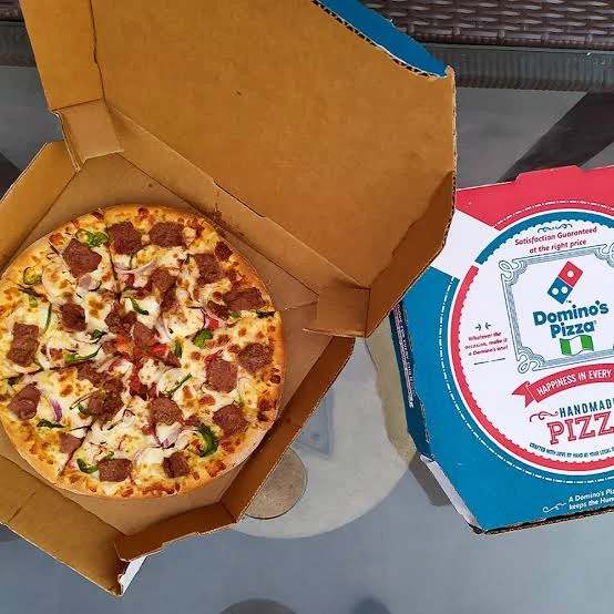 A Domino’s pizza topped with beef, peppers and onions in an open delivery box